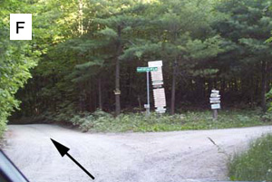 Waypoint F: a second gravel junction with a green street sign and a stack of lane signs, an arrow pointing to the left turn.